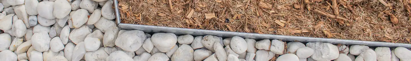 Fresh mulch in a steel-edged bed beside white river pebbles